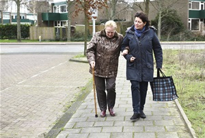 This is a picture of an older lady walking with a cane and linking her arm with a younger lady.