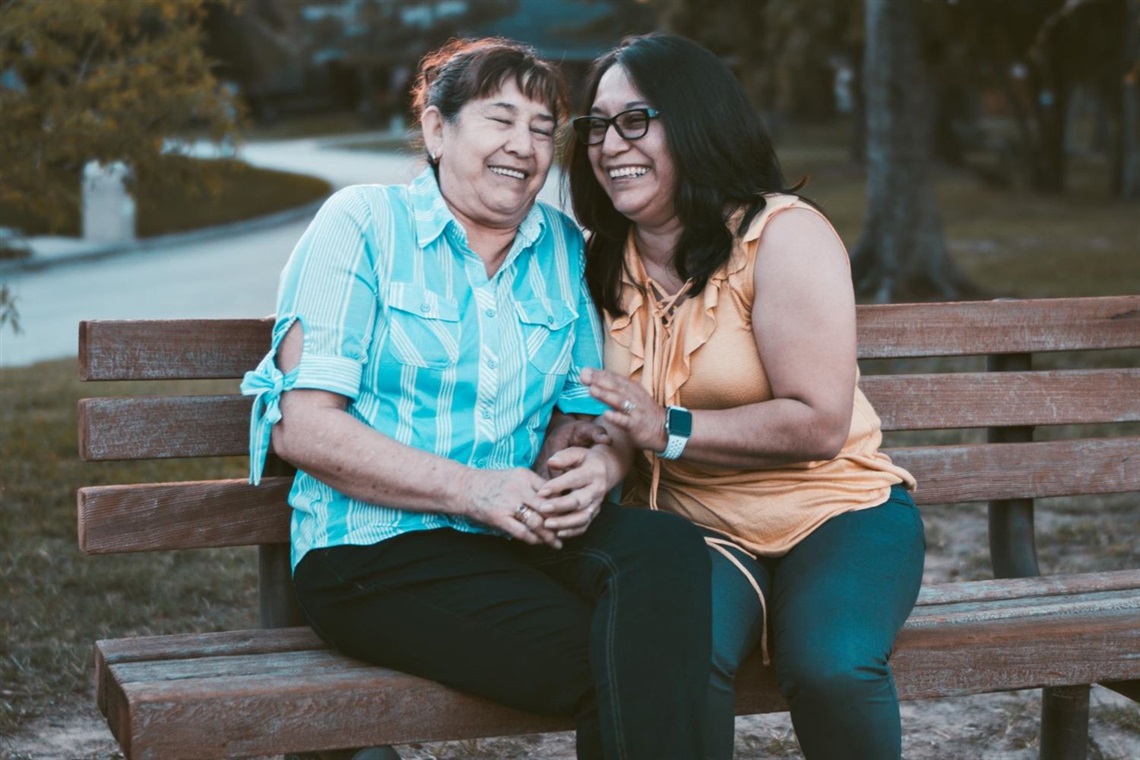 Two women sitting on a bench laughing and embracing